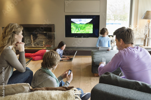 Photo: Family using electronic gadgets in a living room Family using electronic gadgets in a living room