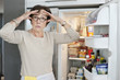 Portrait of an elderly woman looking shocked in front of a refrigerator