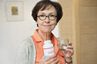 Elderly woman holding bottle of food supplement in the kitchen