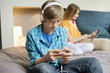 Teenage boy listening to music on iPod with his sister using digital tablet