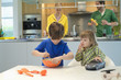 Little girl with a toy car looking at his brother cooking in the kitchen