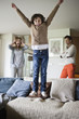 Naughty boy jumping on couch with his parents in the background
