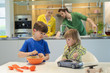 Little girl with a toy car looking at his brother cooking in the kitchen