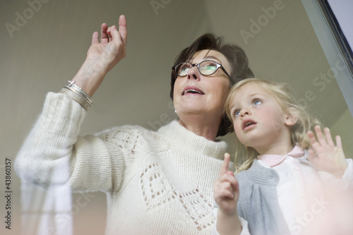 Photo: Woman with her granddaughter looking through a window Woman with her granddaughter looking through a window