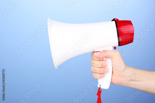 Photo: red and white megaphone in hand on blue background red and white megaphone in hand on blue background