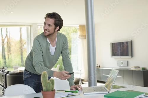 Photo: Man holding a mobile phone and working on a laptop Man holding a mobile phone and working on a laptop