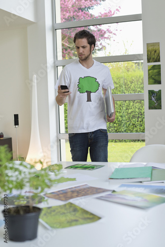 Photo: Man using a mobile phone with environment related posters in front of him on a table Man using a mobile phone with environment related posters in front of him on a table
