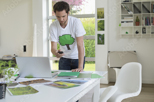 Photo: Man holding a mobile phone and working on a laptop Man holding a mobile phone and working on a laptop