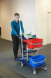 Male cleaner pushing trolley with cleaning equipment