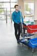 Male cleaner pushing trolley with cleaning equipment