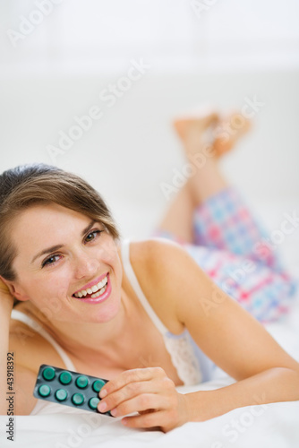 Foto: Happy woman laying on bed with pack of pills Happy woman laying on bed with pack of pills