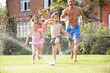 Photo: Family Running Through Garden Sprinkler Family Running Through Garden Sprinkler