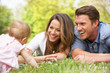 Parents With Baby Girl Sitting In Field Of Summer Flowers