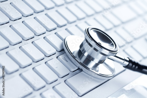 Photo: Silver stethoscope lying down on an laptop, toned blue Silver stethoscope lying down on an laptop, toned blue