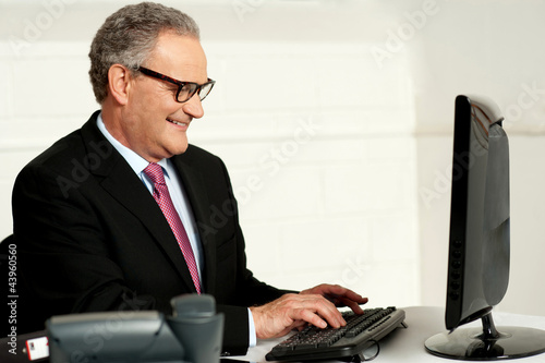 Photo: Cheerful aged man working on computer Cheerful aged man working on computer