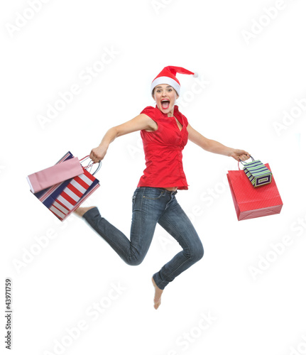 Foto: Happy woman in Christmas hat with shopping bags jumping Happy woman in Christmas hat with shopping bags jumping