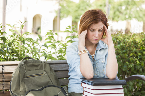 Photo: Female Student Outside with Headache Sitting with Books and Back Female Student Outside with Headache Sitting with Books and Back