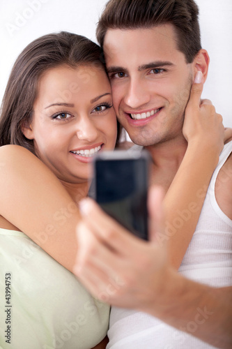 Photo: Smiling couple taking a picture with mobile phone Smiling couple taking a picture with mobile phone