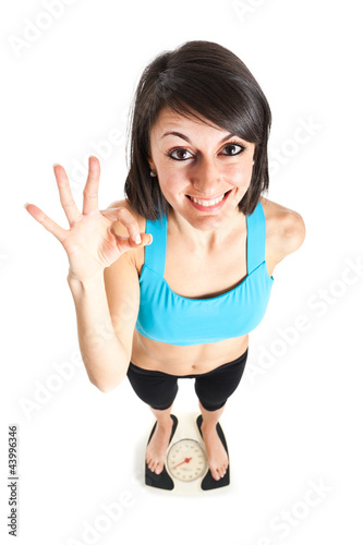Photo: Fitness woman showing ok on a weighing scale Fitness woman showing ok on a weighing scale