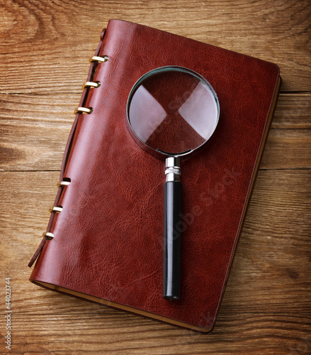 Photo: Notebook with a magnifier on wood table Notebook with a magnifier on wood table