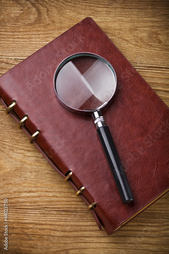 Photo: Notebook with a magnifier on wood table Notebook with a magnifier on wood table