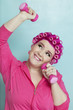 Playful young woman lifting weights over colored background
