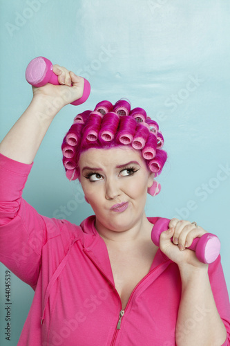 Photo: Young woman making face while lifting dumbbell over colored background Young woman making face while lifting dumbbell over colored background