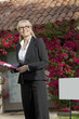 Photo: Happy senior real estate agent looking away with house in background Happy senior real estate agent looking away with house in background