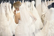 Foto: Back view of a young woman in wedding dress looking at bridal gowns on display in boutique Back view of a young woman in wedding dress looking at bridal gowns on display in boutique