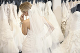 Photo : Back view of a young woman in wedding dress looking at bridal gowns on display in boutique Back view of a young woman in wedding dress looking at bridal gowns on display in boutique