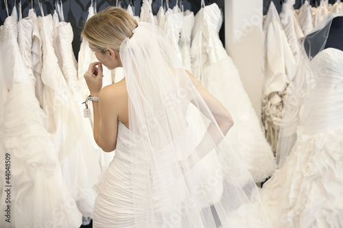 Photo: Back view of a young woman in wedding dress looking at bridal gowns on display in boutique Back view of a young woman in wedding dress looking at bridal gowns on display in boutique