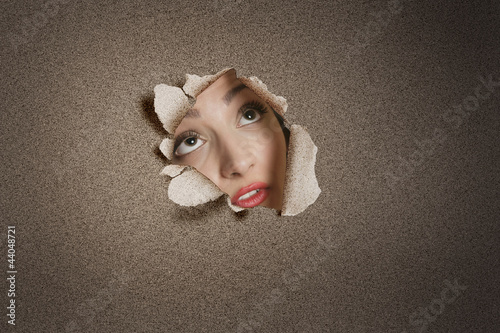 Photo: Young Middle eastern woman looking up from ripped paper hole Young Middle eastern woman looking up from ripped paper hole