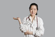 Photo: Portrait of an Asian female doctor displaying an invisible product over gray background Portrait of an Asian female doctor displaying an invisible product over gray background