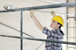 Back view of female contractor placing iron rod on scaffold