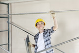 Photo: Mid adult female architect looking up while standing under scaffold at construction site Mid adult female architect looking up while standing under scaffold at construction site