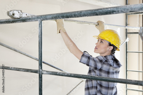 Photo: Back view of female contractor placing iron rod on scaffold Back view of female contractor placing iron rod on scaffold