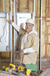 Photo: Portrait of a mature male construction worker checking electric meters at construction site Portrait of a mature male construction worker checking electric meters at construction site