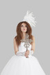 Young brunette bride in wedding gown holding crucifix while looking up over light gray background
