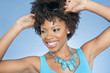 Happy African American woman adjusting sunglasses while looking away over colored background