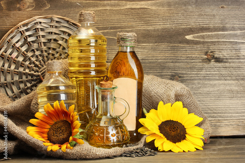 Photo: oil in bottles, sunflowers and seeds, on wooden background oil in bottles, sunflowers and seeds, on wooden background