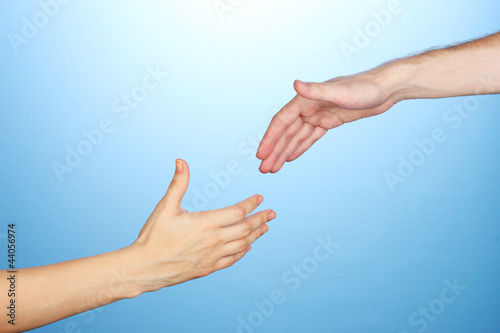 Photo: Women's hand goes to the man's hand on blue background Women's hand goes to the man's hand on blue background