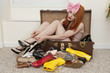 Young woman with bow headband tying footwear while sitting in suitcase