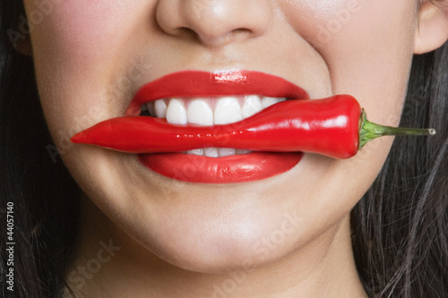 Photo: Close-up portrait of Hispanic woman biting red pepper Close-up portrait of Hispanic woman biting red pepper