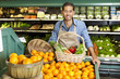 Photo: Portrait of man in supermarket with vegetable basket standing near oranges stall Portrait of man in supermarket with vegetable basket standing near oranges stall