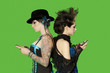 Photo: Side view of punk females standing back to back over with mobile phones over green background Side view of punk females standing back to back over with mobile phones over green background
