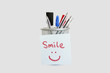 Photo: Close-up of adhesive notepaper with smiley face stuck on pen holder over white background Close-up of adhesive notepaper with smiley face stuck on pen holder over white background