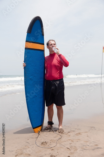 Photo: man the surfer to stand on a beach and drinks water man the surfer to stand on a beach and drinks water