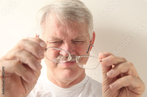 Photo: an older man squints at his glasses an older man squints at his glasses