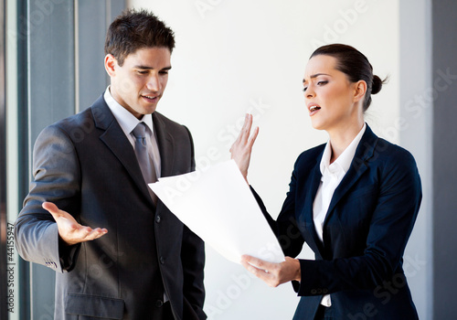Photo: two young colleagues arguing over paperwork in office two young colleagues arguing over paperwork in office