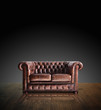 Classic Brown leather sofa on wood in darkroom background.